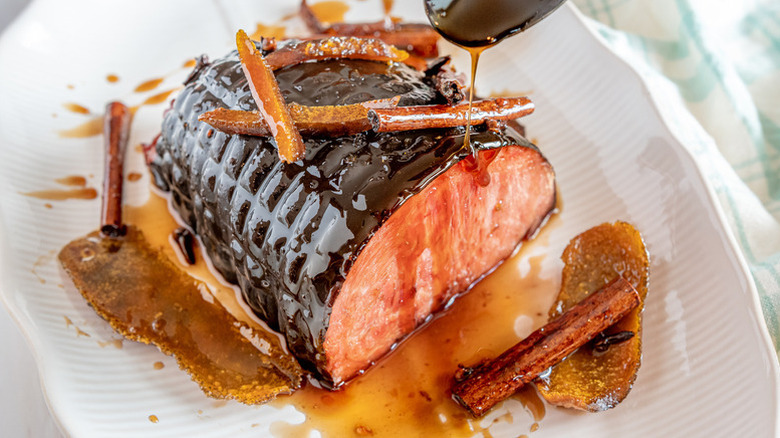 Spooning glaze over sticky baked ham on serving plate
