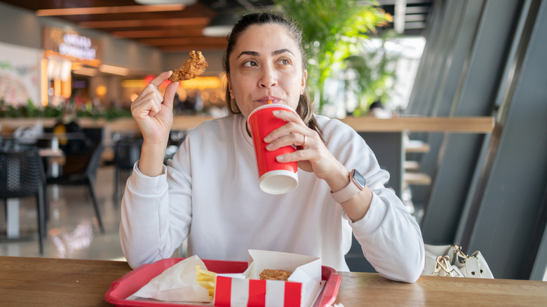 woman sipping on a drink and eating fast food in a food court