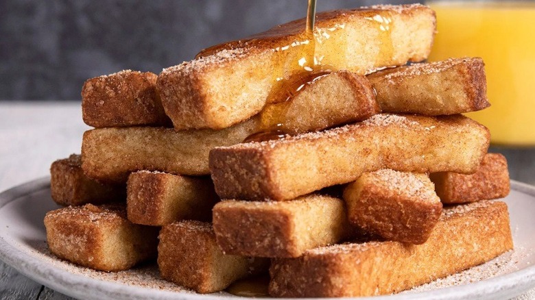 Maple syrup being poured over a plate piled high with French toast sticks