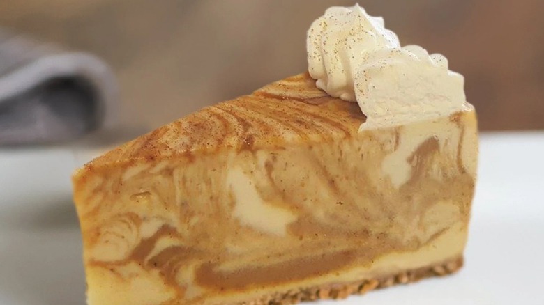 Single slice of cheesecake swirled with pumpkin and topped with whipped cream