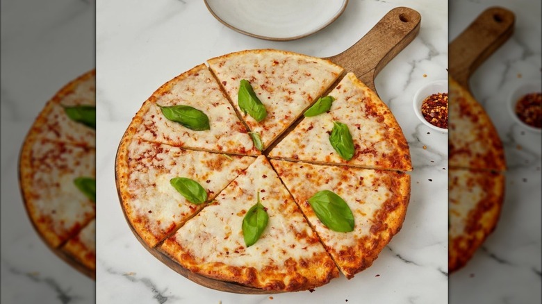 Pizza on wooden serving platter on countertop with red chili flakes scattered around