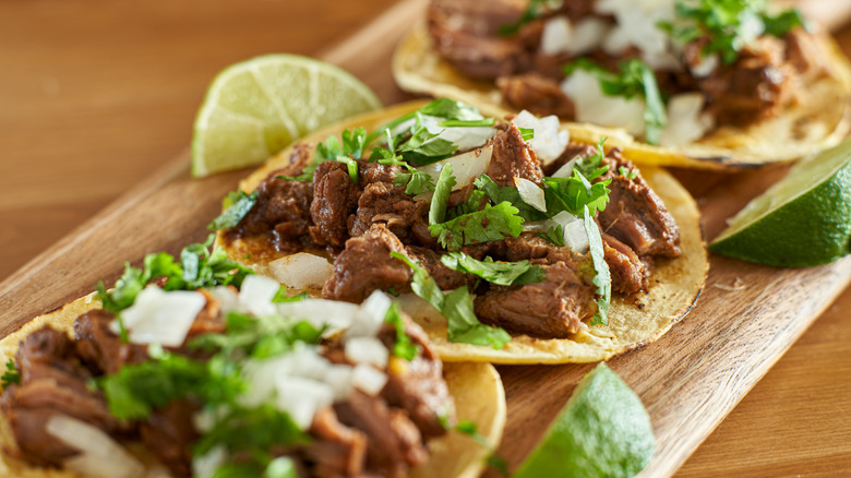 carne asada three mexican grill tacos on a wooden platter with limes