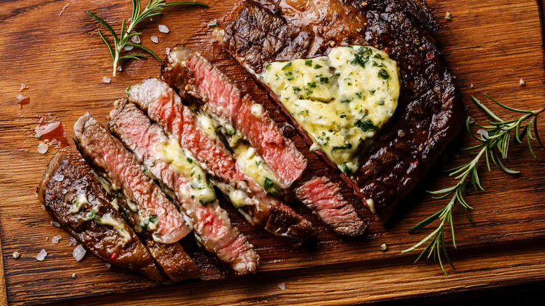 medium rare ribeye steak cut in strips topped with herb butter on a wooden tray