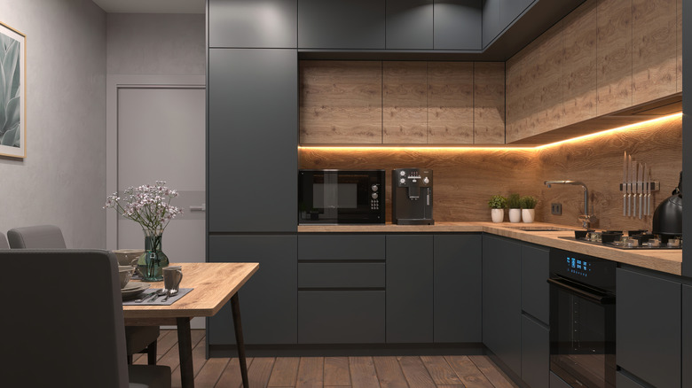 A kitchen with black painted cabinets and drawers with wood floor and backsplash
