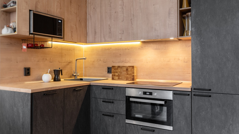 A dark kitchen with a wood backsplash and lighting underneath the upper cabinets