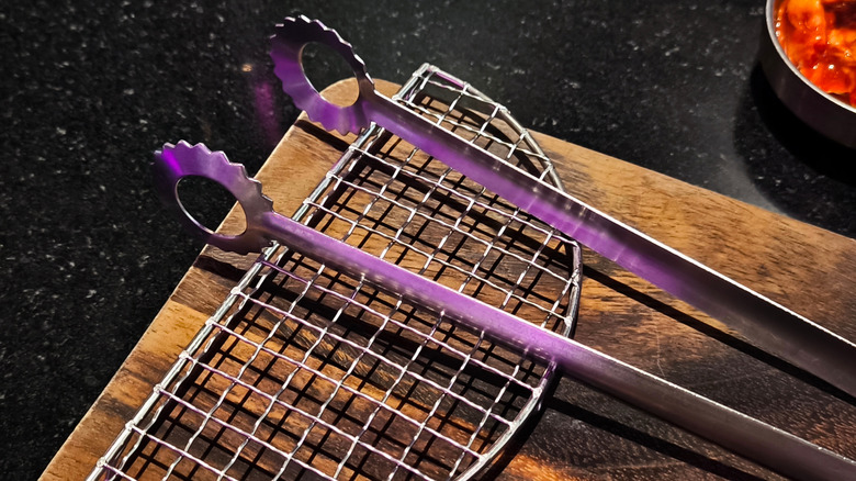 Barbecue grill and tongs placed on wooden cutting board