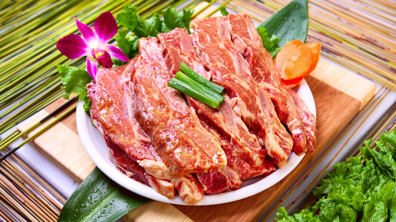 Raw marinated beef placed on a plate with floral and leafy garnish