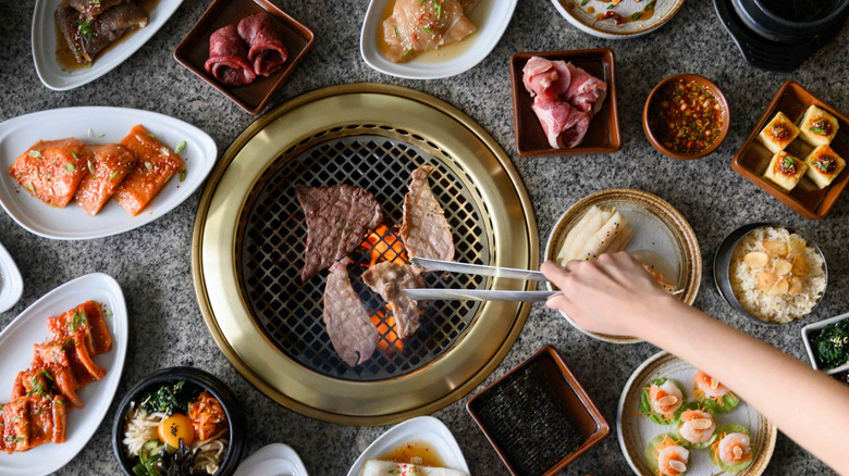 Hand grilling meat alongside an array of side dishes at a Korean BBQ restaurant