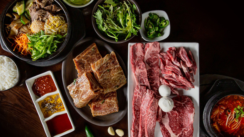 Korean BBQ table featuring marinated meats and a large array of side dishes