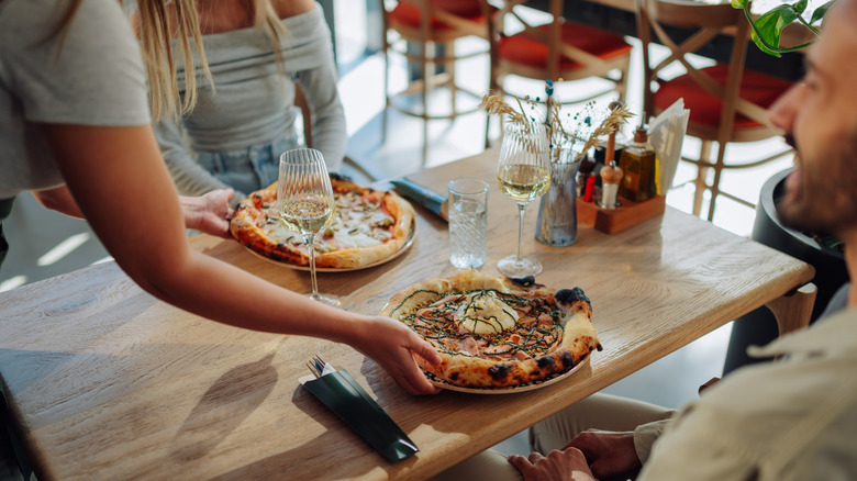 Waitress' arms setting pizza down in front of diners at table