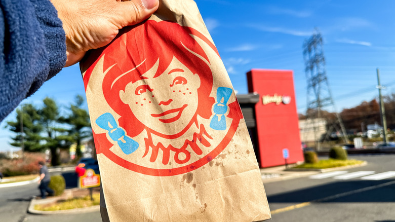 A person holds a brown paper bag with the Wendy's logo