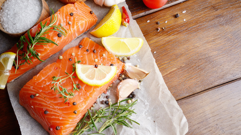 Seasoned raw salmon on parchment paper with lemon slices and herbs