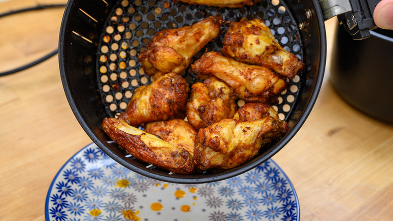 Chicken with sauce being shaken out of an air fryer basket onto a plate