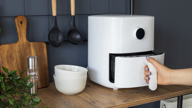 Hand pulling white air fryer basket from machine
