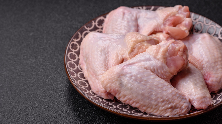Raw chicken wings in brown bowl on black table