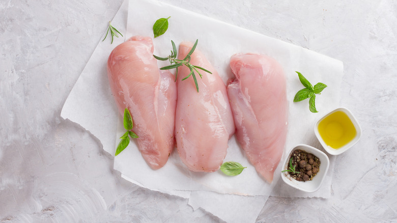 Raw chicken on parchment paper with herbs and olive oil
