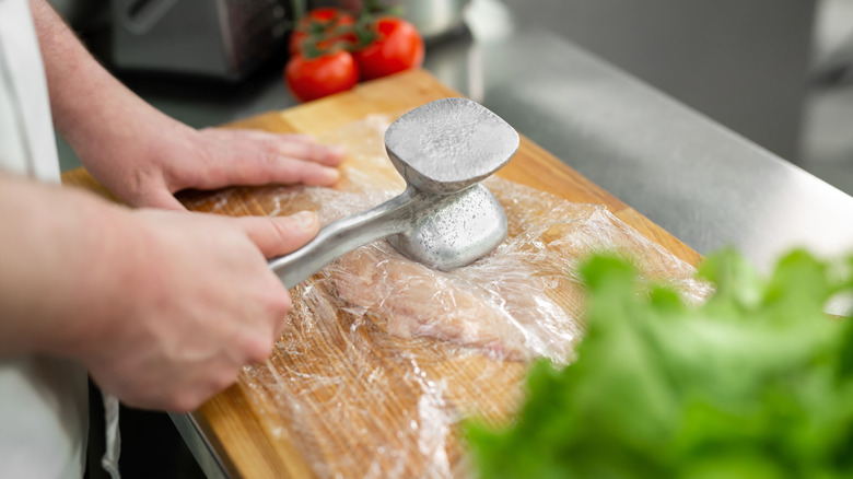 A person pounding a chicken breast with a meat mallet