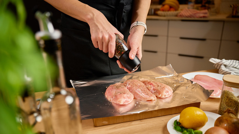 a person cracking pepper over chicken on cutting board
