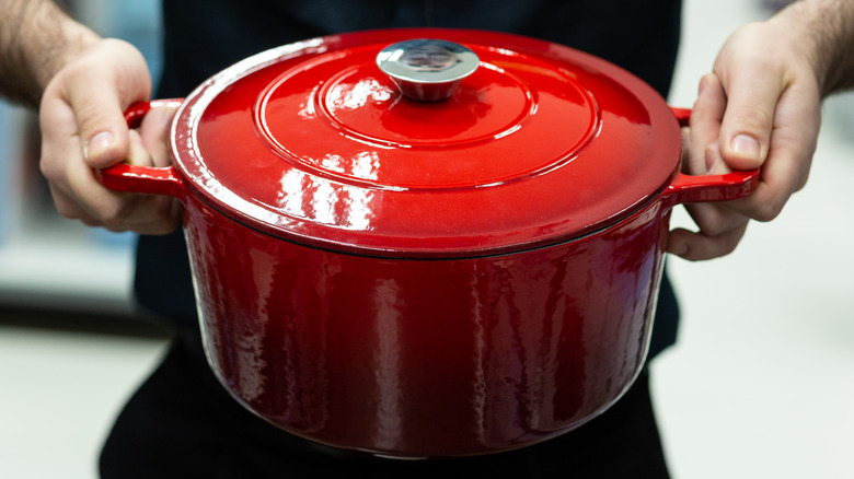 Hands holding red Dutch oven with lid