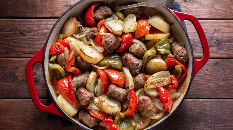 Red Dutch oven crowded with sausage and other ingredients