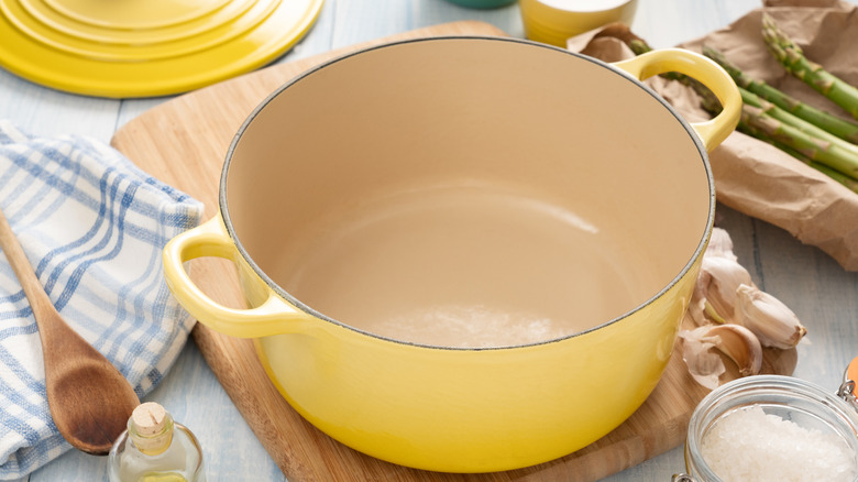 Empty yellow Dutch oven on wooden cutting board