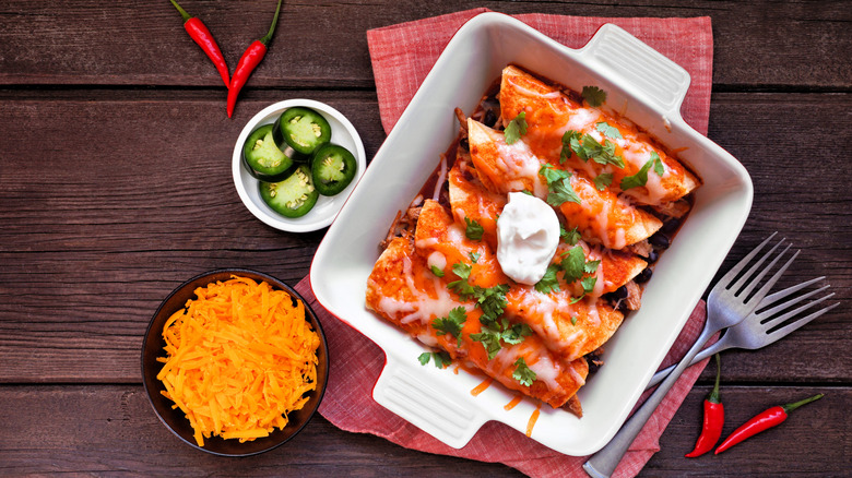Chicken enchiladas in baking dish with cheese and jalapenos on the side