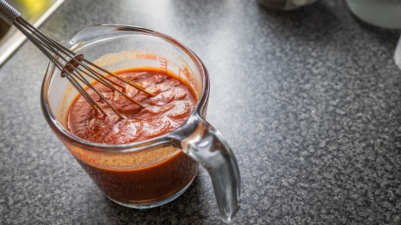 Enchilada sauce in glass measuring cup with whisk