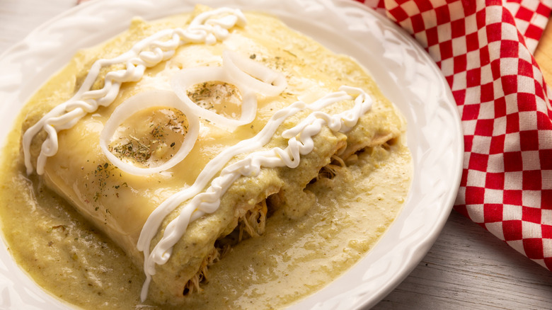 Green chicken enchiladas with a lot of sauce on white plate