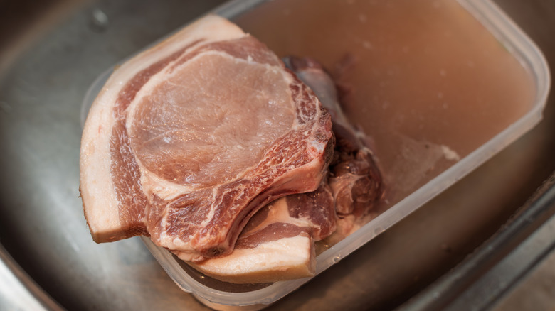 raw pork chops and brine, in a plastic food storage container, resting in a stainless-steel sink