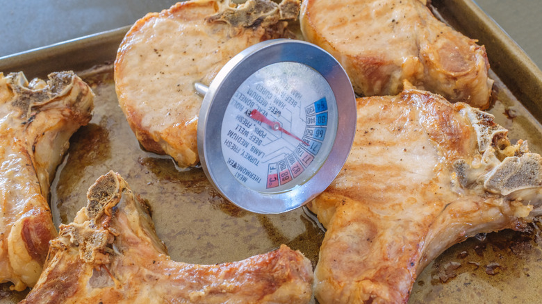baked pork chops on a sheet pan, with a meat thermometer in one showing it cooked to the old-school temperature of 160°F