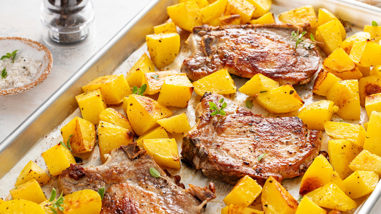 pork chops and golden potatoes, roasted together on a sheet pan, with a pepper grinder and a small dish of herbed salt visible to the left of the sheet pan