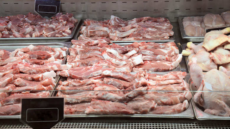 pans of uncooked pork chops in a retail meat display counter, with some chicken cuts visible as well at the edge of the frame on the right