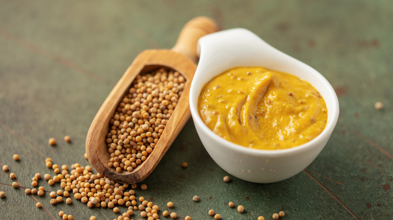 Spicy mustard in a white bowl on a table with mustard seeds in a wooden scoop