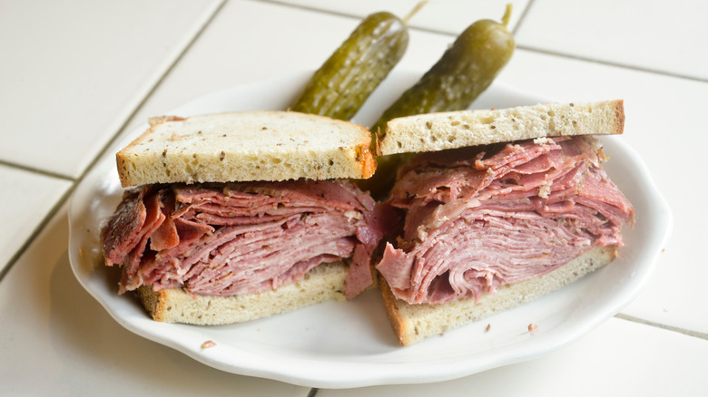 Corned beef and tongue sandwich with half-sour pickles on a white plate