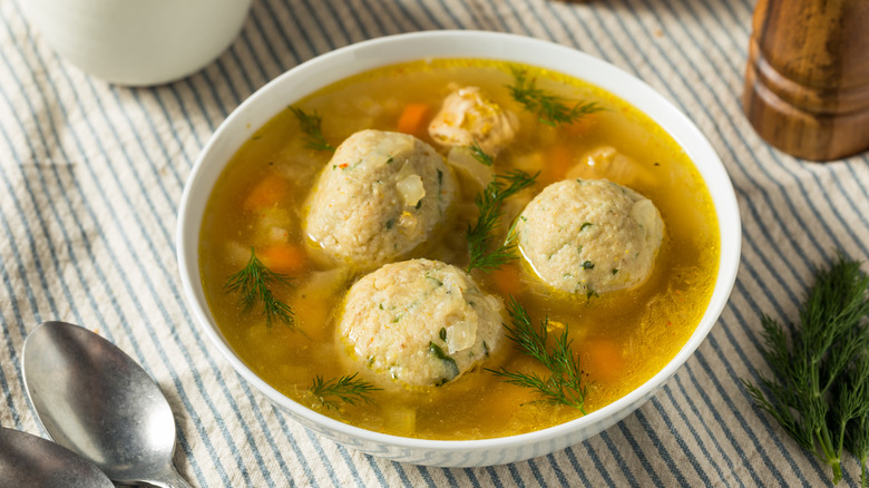 Matzo ball soup in a white bowl on a striped tablecloth