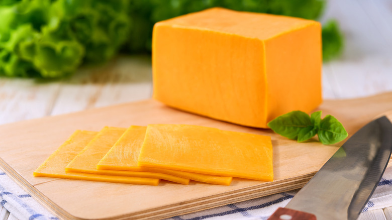 Sliced yellow cheese and knife on a wooden board