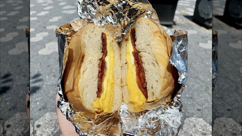 Hand holding a bacon, egg, and cheese bagel in foil on a NYC sidewalk