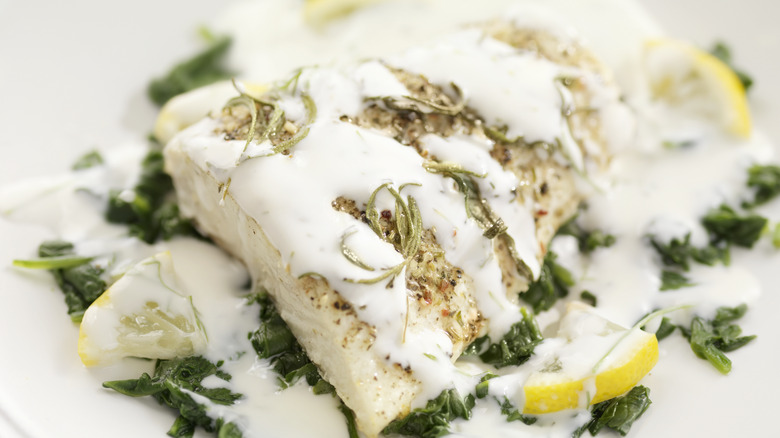 A fish dish with lemon and herbs covered in a white sauce