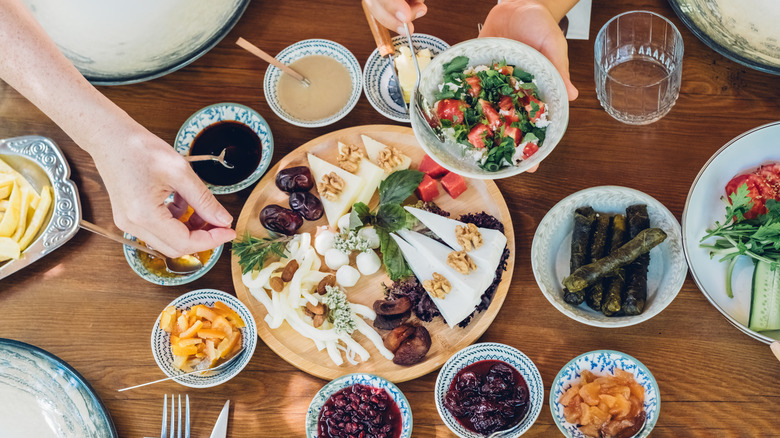 Hands grabbing foods from a spread of meze on a wood table