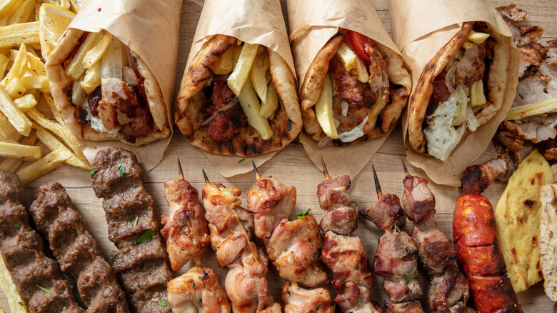 Four Greek gyros and souvlaki meats arranged on a wood platter