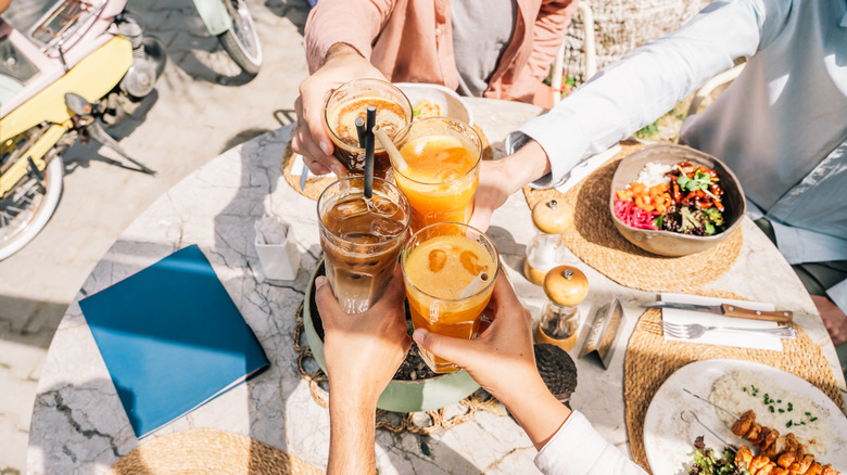 Four people cheers with various drinks over a table of Greek dishes