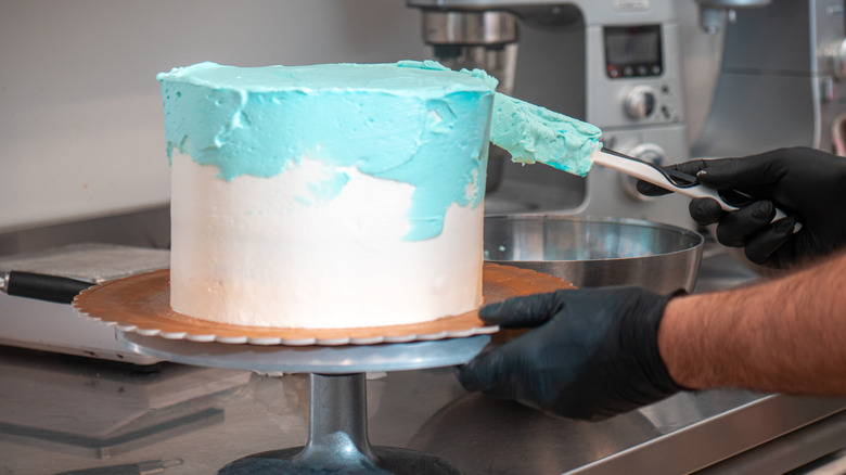 Person spreading blue frosting on cake