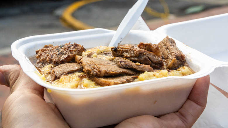Hand holding a bowl of brisket and grits