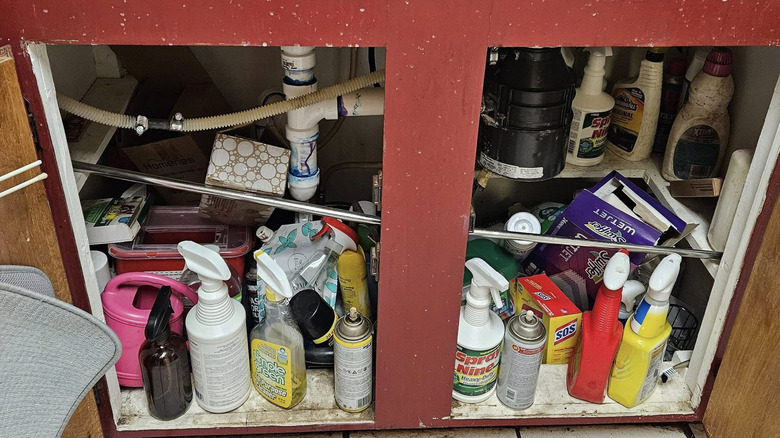 Different tools and supplies in open cabinet under messy sink
