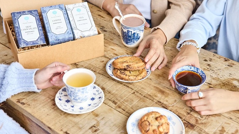 Three people enjoying coffee, tea, and hot chocolate alongside cookies at wooden table
