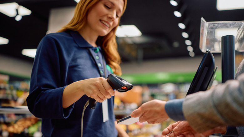 Close up of cashiers scanning coupon on customer's cell phone at supermarket checkout.