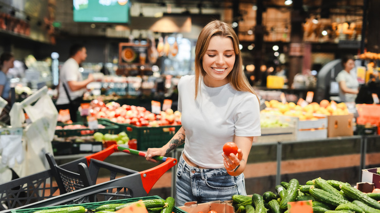 woman is smiling while choosing a tomato in the vegetable aisle