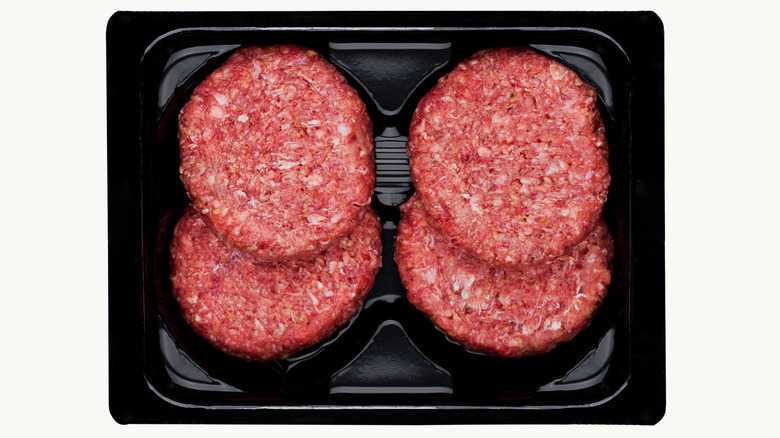 Raw fresh beef burgers in plastic tray on white background