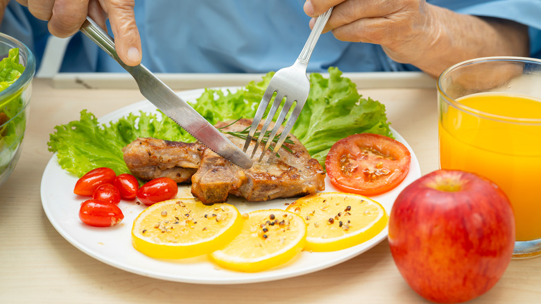 elderly person eating a pork steak with salad and fruit as a healthy hospital meal