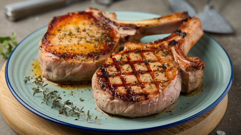 two thick pork rib chops, one grilled and one apparently pan-seared, on a blue-green plate with a sprig of thyme